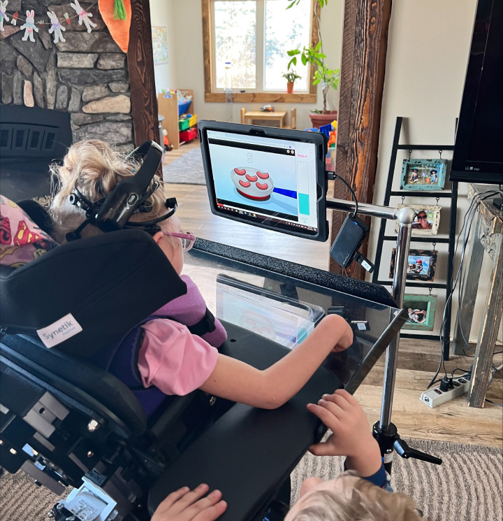 Claire sits in her wheelchair in front of a computer screen, interacting with the image on screen through her BCI headset.