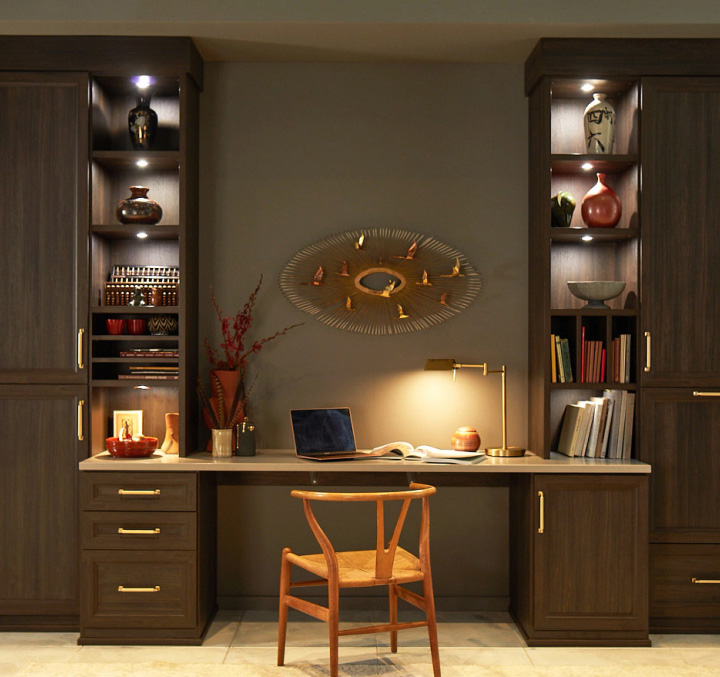 A wide desk with bookcases on either side and lighting on each shelf.