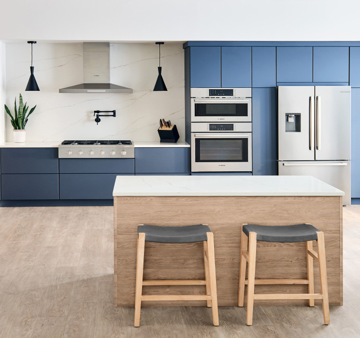 A sleek, modern kitchen with blue cabinets with no door handles, an island and two stools.