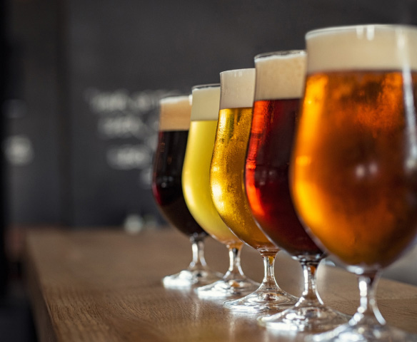 A flight of different coloured beers in tall glasses.
