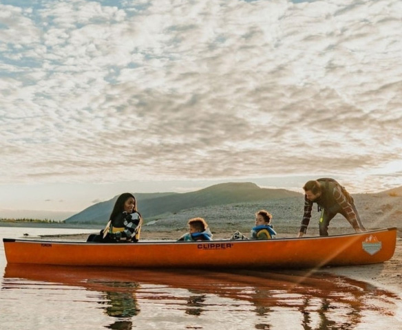 An orange Canoe with a family inside, juxtaposed against a cloudy sunset.