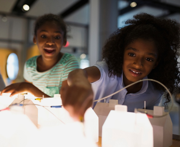 Two children participate in an experiment, lit from below by glowing lights.